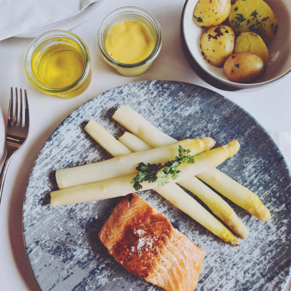 Bild von weißem Spargel und Lachs, serviert mit Sauce Hollandaise. Ein klassisches Mittagsgericht zur Spargelzeit.